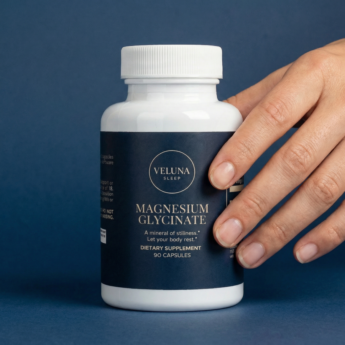 Veluna Magnesium Glycinate Capsules bottle on a navy blue backdrop with a hand resting on its side
