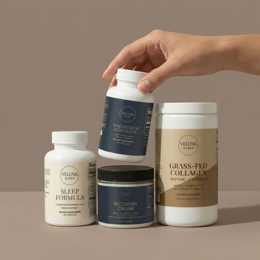 Veluna Deep Restore Full Bundle on taupe, a hand lifting the Magnesium Glycinate bottle off the Recovery Cream jar