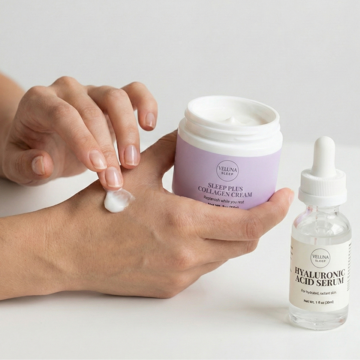 Veluna Sacred Soothe Starter Bundle, fingers spreading night cream on the back of a hand, serum bottle beside