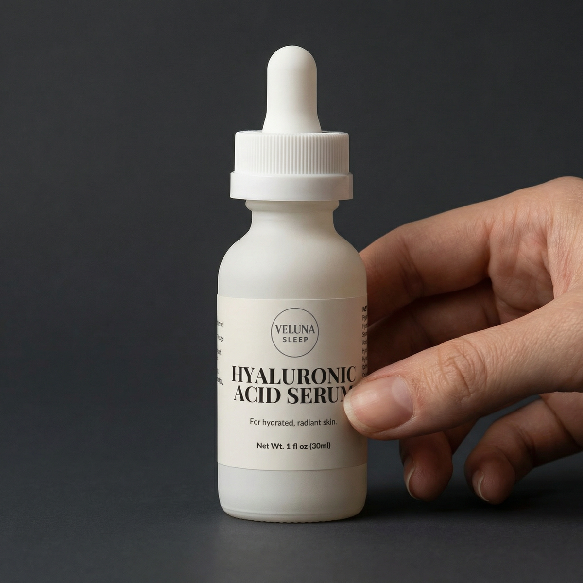 Veluna Hyaluronic Acid Serum in a white dropper bottle against a charcoal backdrop, held between fingers