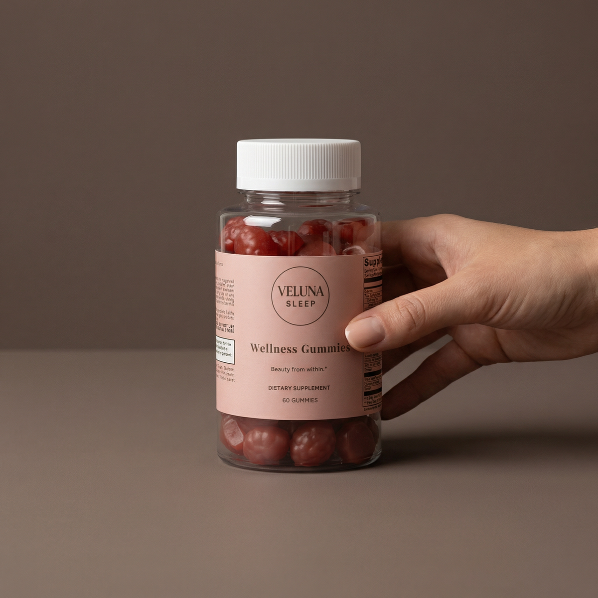 Veluna Hair, Skin & Nails Gummies jar on a taupe backdrop, held at the side by one hand