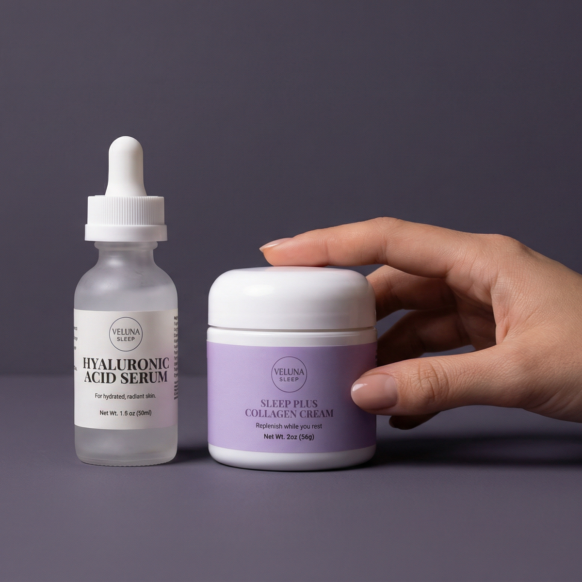 Veluna Sacred Soothe Starter Bundle on a violet-grey backdrop, a hand on the night cream lid beside the serum