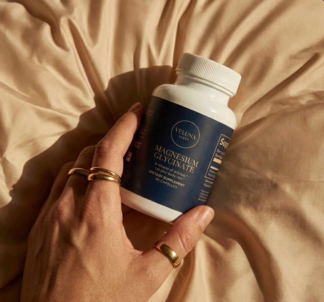 Veluna Magnesium Glycinate Capsules bottle held in a hand wearing gold rings over beige bedding
